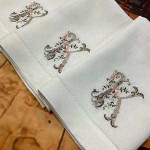May include: Three white linen tea towels with embroidered floral designs and the letter 'A' in a script font.