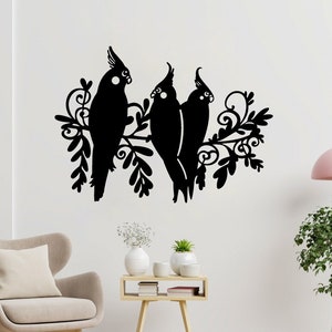 May include: Black silhouette of three cockatiels perched on a branch with stylized leaves. The birds are facing different directions and have detailed features. The silhouette is on a white wall with a light fixture and a potted plant in the background.