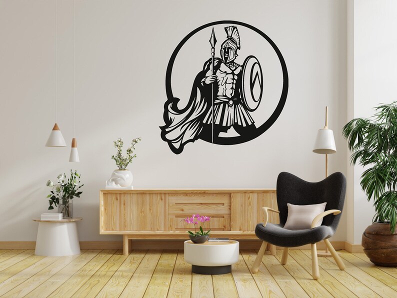 Puede incluir: Silueta en blanco y negro de un guerrero sosteniendo una lanza y un escudo en un marco circular. El guerrero lleva un casco y una armadura. La imagen est&aacute; en una pared blanca con un armario de madera y una silla en el fondo.