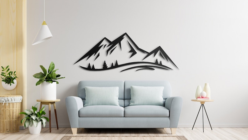 May include: Black metal wall art depicting a mountain range with trees in front. The art is mounted on a white wall above a light blue sofa.