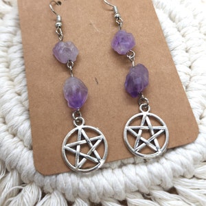 May include: A pair of dangle earrings featuring raw amethyst stones and silver-toned pentacle charms. The earrings are suspended from silver-colored ear wires. The product card reads "THE MUSHROOM MINNEAPOLIS MN".