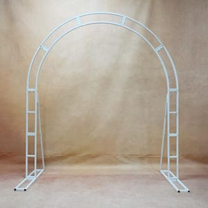 May include: A white metal wedding arch with a rounded top and rectangular base. The arch is constructed from connected rectangular and curved metal pieces, creating a sturdy frame for outdoor or indoor events. The arch is designed to be freestanding.