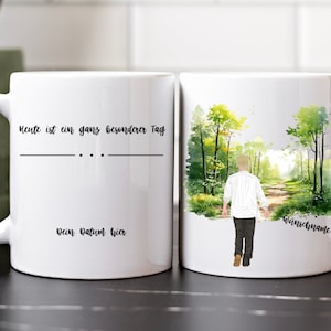 May include: White ceramic mug with a watercolour design of a person walking through a forest. The text "Heute ist ein ganz besonderer Tag" is on the mug.