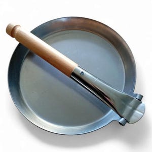 Könnte beinhalten: Eine runde, silberfarbene Pfanne mit einem Holzgriff. Die Pfanne hat einen klappbaren Deckel, der am Griff befestigt ist.