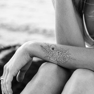 May include: Black and white floral temporary tattoo applied to the forearm. The tattoo features a bouquet of roses, peonies, and other flowers with detailed line art. The design is a delicate and elegant floral arrangement.