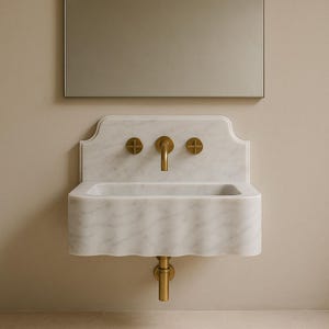 May include: A white marble sink with a wavy edge and a gold tap. The sink is mounted on a white marble wall with a gold trim. The tap has two gold knobs on either side.
