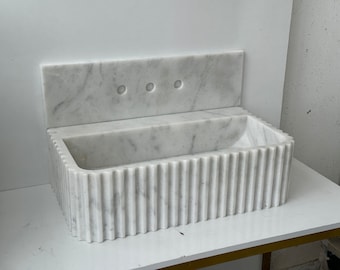 May include: White marble bathroom sink with a fluted design and a matching backsplash with three holes.