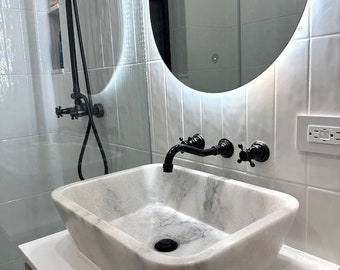 Puede incluir: Un lavabo de baño de mármol blanco con un grifo y un desagüe negros. El lavabo está montado en una encimera blanca.