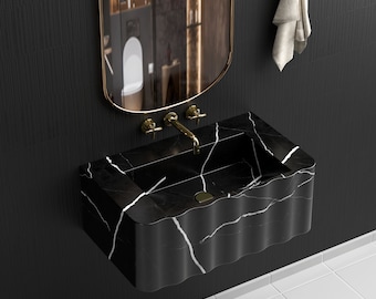 Könnte beinhalten: Ein schwarzes Marmorwaschbecken mit wellenförmigem Rand und weißen Adern. Das Waschbecken ist an einer schwarzen Wand mit goldenen Armaturen montiert.