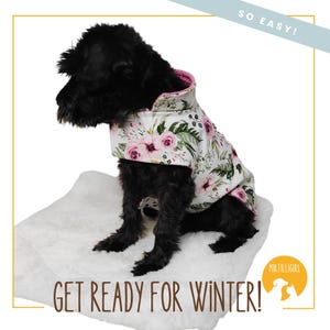 May include: A black dog wearing a white and pink floral dog coat with a pink lining. The dog is sitting on a white fluffy surface. The text "SO EASY!" is in the upper right corner of the image. The text "GET READY FOR WINTER!" is in the lower left corner of the image. The text "MIR TILLIGIRL" is in the lower right corner of the image.