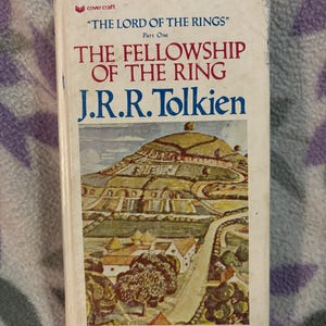 May include: A well-worn copy of "The Fellowship of the Ring" by J.R.R. Tolkien. The book's cover displays a landscape illustration and the title, part of "The Lord of the Rings" series. The cover is slightly faded.