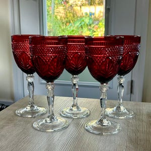 May include: A set of five deep red glass goblets featuring a textured diamond pattern on the upper bowl and a leaf-like design on the lower bowl. Each goblet has a clear, faceted glass stem and a round, transparent base for stability.