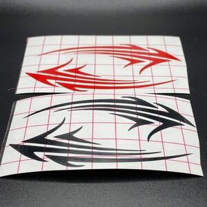 Pu&ograve; includere: Due fogli di carta adesiva bianca con disegni in stile tribale nero e rosso. I disegni sono su uno sfondo bianco con un motivo a griglia.