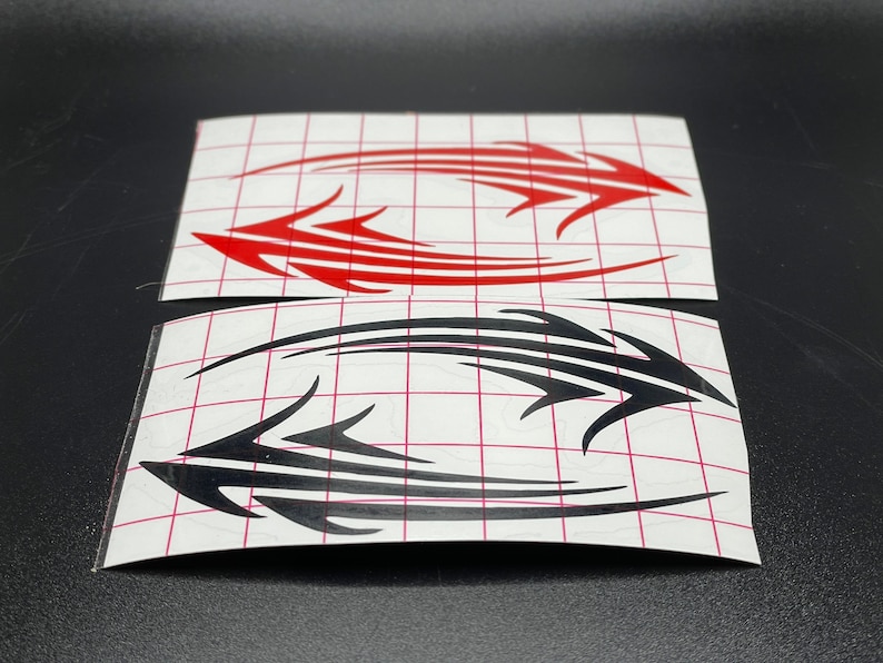 Pu&ograve; includere: Due fogli di carta adesiva bianca con disegni in stile tribale nero e rosso. I disegni sono su uno sfondo bianco con un motivo a griglia.