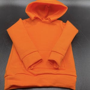 May include: Bright orange hoodie with a hood and a front pocket. The long-sleeved sweatshirt has ribbed cuffs and a ribbed hem. The garment is made of a soft, comfortable material.