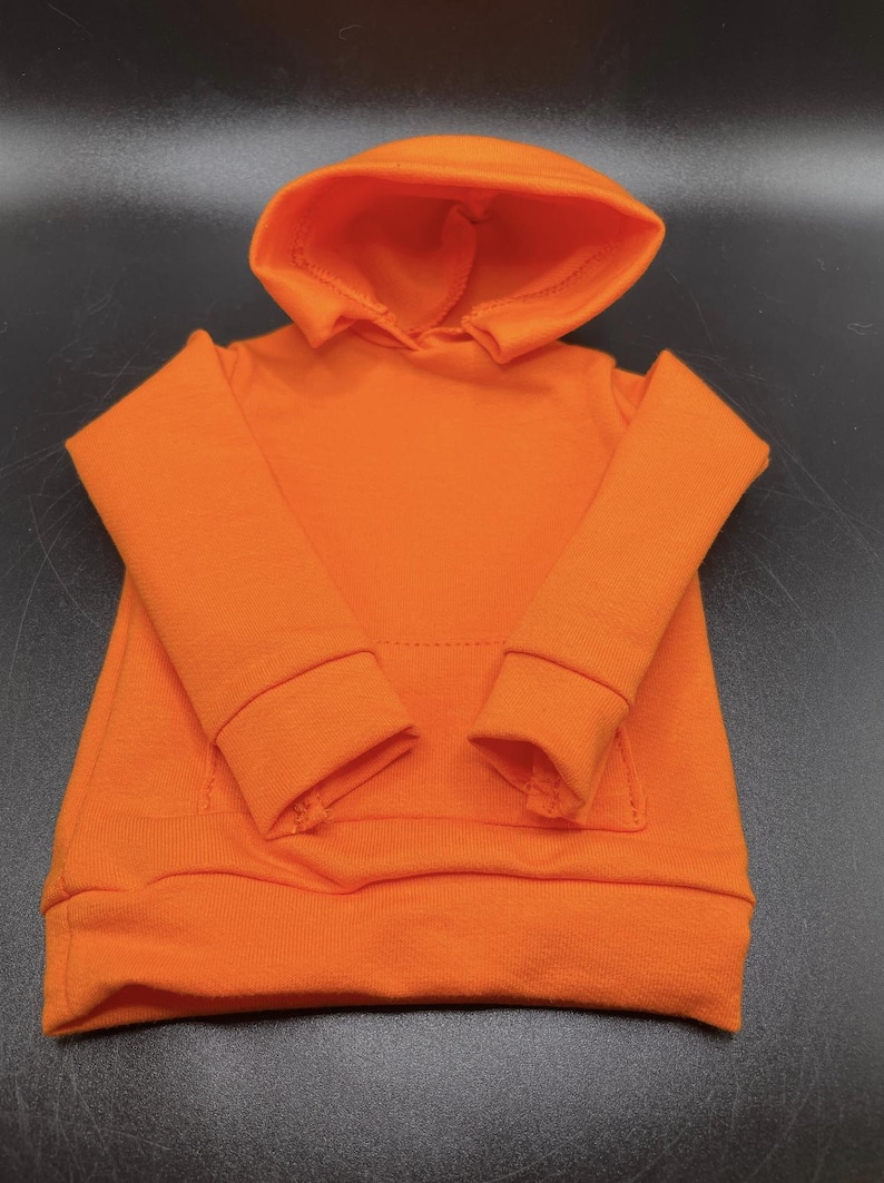 May include: Bright orange hoodie with a hood and a front pocket. The long-sleeved sweatshirt has ribbed cuffs and a ribbed hem. The garment is made of a soft, comfortable material.
