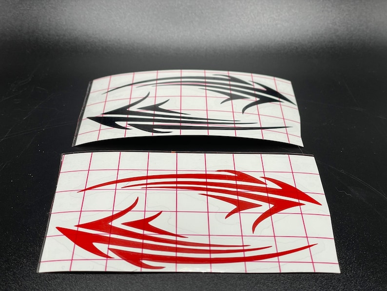 Pu&ograve; includere: Due fogli di carta adesiva bianca con disegni in stile tribale nero e rosso. I disegni hanno la forma di frecce e sono su uno sfondo a griglia.