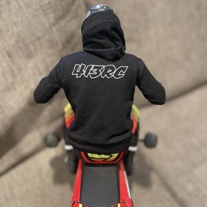 May include: A black hoodie with the text "413RC" on the back is worn by a figure on a red and black toy motorcycle. The motorcycle has yellow and red accents and the text "FXR" on the rear.