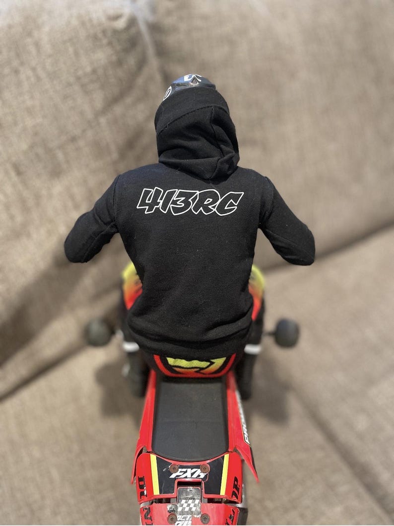 May include: A black hoodie with the text "413RC" on the back is worn by a figure on a red and black toy motorcycle. The motorcycle has yellow and red accents and the text "FXR" on the rear.