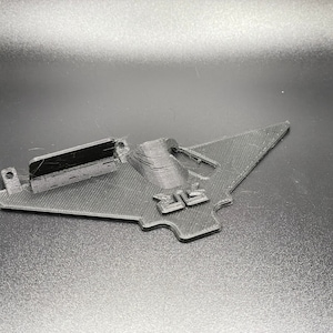 May include: A black 3D printed object shaped like a plane with the word "BIG" printed on it.