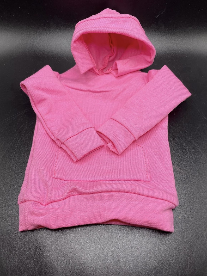 May include: A bright pink hooded sweatshirt with long sleeves and a kangaroo pocket. The sweatshirt is made of a soft, knit fabric and features a drawstring hood and ribbed cuffs and hem.