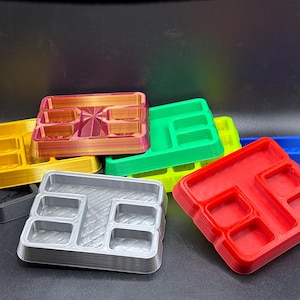 May include: A collection of colorful, 3D-printed trays in various colors, including red, green, yellow, and blue. Each tray has multiple compartments of different sizes, ideal for organizing small items. The trays are made of plastic.