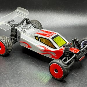 May include: A silver and red remote control race car with a clear spoiler and red wheels. The car has a flame design on the side and yellow accents.