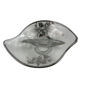 Op de afbeelding: Een heldere glazen serveerschaal met een zilveren rand en bloemmotief. De schaal heeft een unieke vorm met een centraal gedeelte voor dips of sauzen. Het bloemmotief is zilverkleurig en voegt elegantie toe.