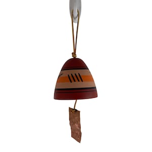 May include: A decorative wind chime with a bell-shaped body. The bell is painted with horizontal stripes of orange, tan, and dark red. Black diagonal lines are painted on the bell. A small copper tag hangs from the bottom.