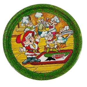 May include: A circular, green metal tray with a festive design. The tray depicts a cartoon scene of Keebler elves baking, with the word "Goodness" on a sign. The border is decorated with green leaves and red berries.