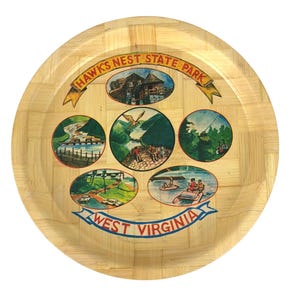 Puede incluir: Una bandeja redonda de madera con un patrón tejido. La bandeja presenta una ilustración colorida del Parque Estatal Hawks Nest en West Virginia. La ilustración incluye imágenes de un albergue, un río, un sendero para caminatas, un mirador y un lago.