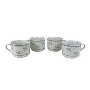 May include: Four white ceramic mugs with a blue scalloped border and green leaf pattern. Two mugs have handles, and two are handleless. The mugs are arranged on a white background.