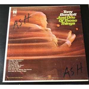 May include: Vintage vinyl record album cover for Tony Bennett's "Just One of Those Things." The cover features a blurred image of a person and the album title in green and yellow. The album's tracklist is listed on the bottom left.