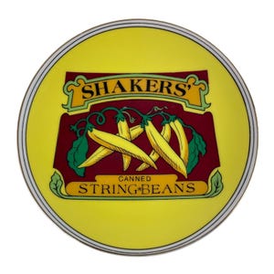 Può includere: Un piatto rotondo giallo con un design decorativo con il testo "SHAKERS" e "CANNED STRING BEANS". Il design include fagiolini gialli su uno sfondo marrone, con un bordo bianco e oro.