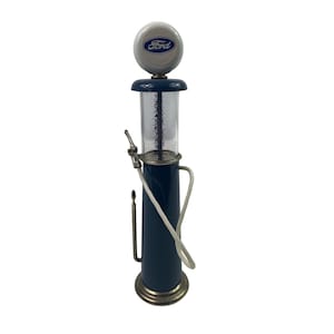 May include: A vintage-style blue and silver gas pump with a white Ford logo on top. The pump has a clear glass cylinder with numbered measurements, a silver nozzle, and a white hose. The base is silver.