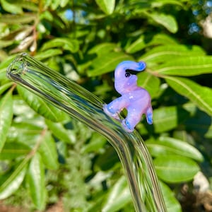 Pu&ograve; includere: Una cannuccia da bere in vetro trasparente con un ciondolo a forma di elefante in vetro viola e blu attaccato alla parte superiore.