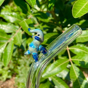 Pu&ograve; includere: Una statuetta di elefante in vetro blu e bianco posata su una cannuccia da bere in vetro trasparente.
