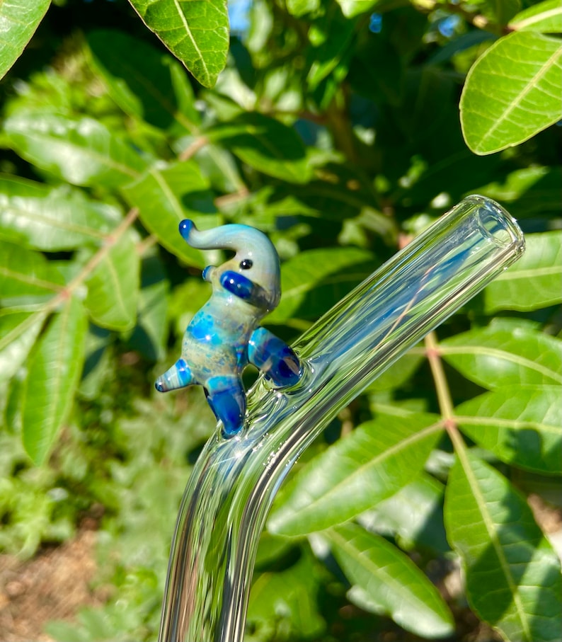 Pu&ograve; includere: Una statuetta di elefante in vetro blu e bianco posata su una cannuccia da bere in vetro trasparente.