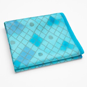May include: Folded turquoise fabric with a grid pattern and small circular accents. The fabric has a gradient of blue hues, with a darker blue border. The grid lines and accents are a metallic silver color.