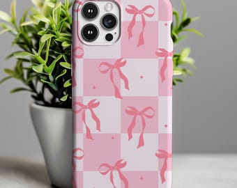 May include: A pink and white checkered phone case with a pattern of pink bows. The case has a glossy finish and a camera cutout. The phone case is shown next to a small potted plant.