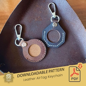 May include: Two leather AirTag keychains with a brown and black color scheme. One keychain is a round shape with a stitched edge and the other is a hexagonal shape with a stitched edge. Both keychains have a silver metal loop for attaching to keys.