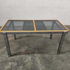May include: A rectangular glass-top dining table with a wood trim around the edge. The table has a silver metal frame and four legs.
