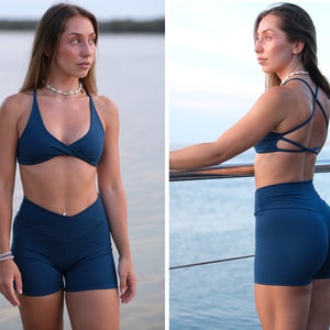 May include: A woman wearing a dark blue sports bra and matching high-waisted shorts. The bra has a criss-cross back and the shorts have a high-cut leg.