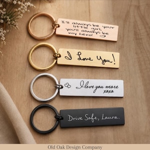 May include: Four rectangular keyrings with various metal finishes. The top keyring is copper-coloured and reads "I'll always be your little girl, you'll always be my hero!". Other keyrings say "I Love You!", "I love you more xoxo", and "Drive Safe, Laura."