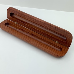May include: A wooden pen case with a hinged lid, made of reddish-brown wood with a smooth finish. The case is open, revealing the empty interior.