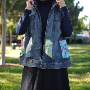 May include: A blue denim vest with a zipper closure and colorful fabric patches on the front pockets.