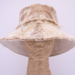 Puede incluir: Un sombrero de cubo beige con un borde deshilachado y un patrón de teñido anudado.