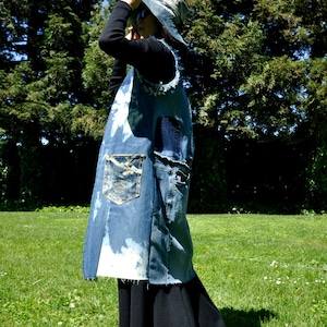 May include: A denim apron-style garment with multiple pockets and a distressed, bleached design. The garment is paired with a matching denim hat. The overall style is casual and unique, suitable for artistic or bohemian aesthetics.