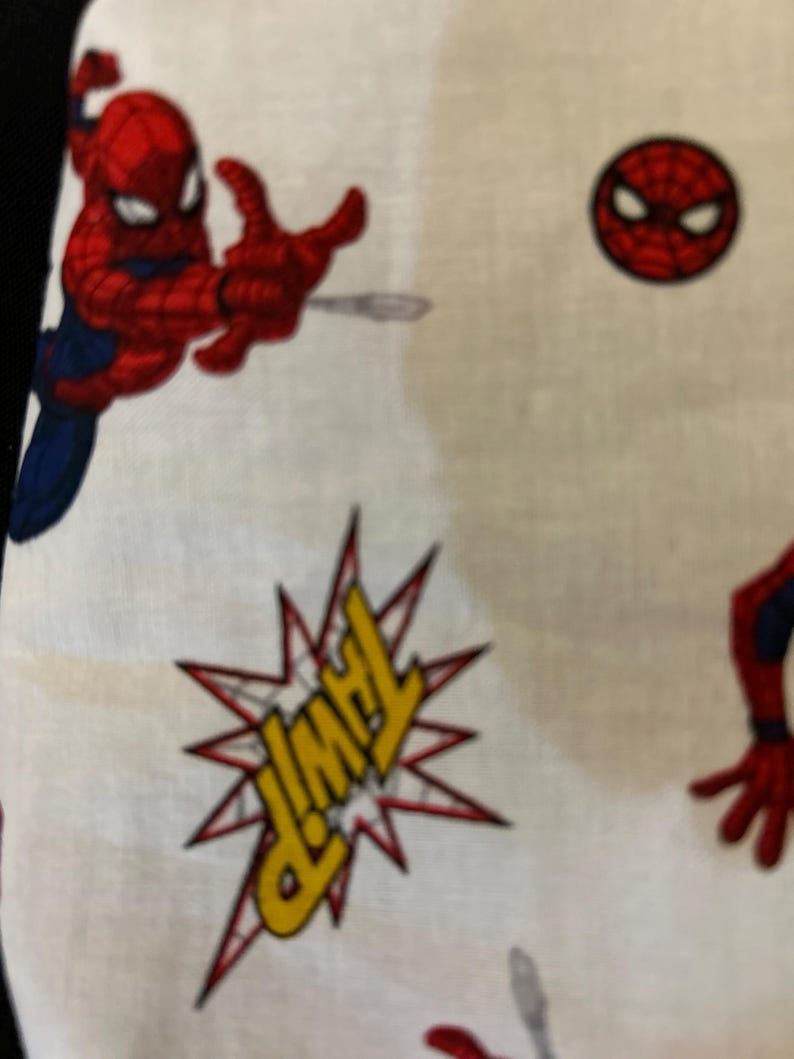 May include: White fabric with a red and blue Spiderman design. The fabric has a repeated pattern of Spiderman in different poses, including a Spiderman head and a speech bubble that says "THWIP".