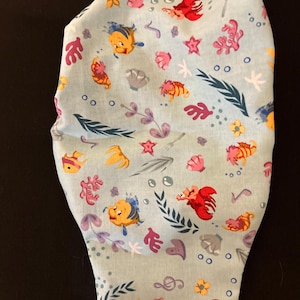 K&ouml;nnte beinhalten: Ein hellblauer Stoff mit einem sich wiederholenden Muster aus gelben und orangefarbenen Fischen, roten Hummern, rosa Muscheln und gr&uuml;nem Seetang. Der Stoff ist perfekt f&uuml;r Bastelprojekte wie Gesichtsmasken.